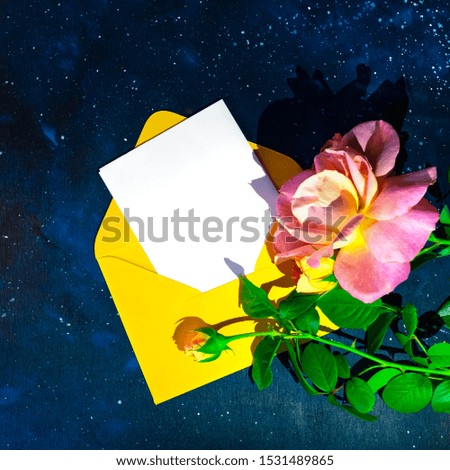 An orange envelope in which a blank white sheet for text, a composition on a dark blue background decorated with flower and a glowing garland. Flat lay.