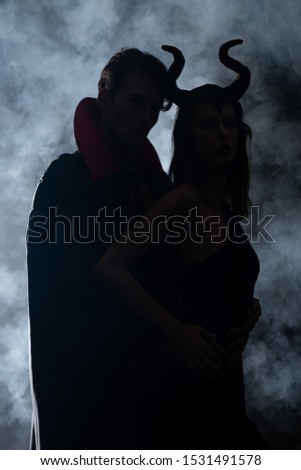 silhouette of man and woman in halloween costumes on black with smoke 
