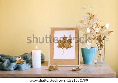Dry yellow and golden flowers in vase, candle, cup and picture frame with golden leaf. Home Decoration details. Design of interior.