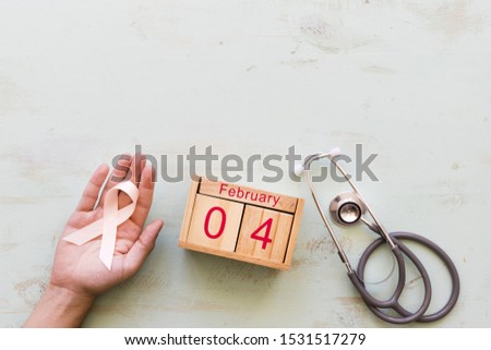 Hand holding awareness ribbon with stethoscope and 4th February wooden box on backdrop