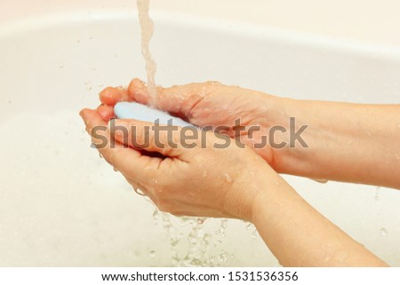 Female hands with soap under the jet of water in the bathroom