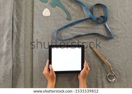 Close-up of tailor holding digital tablet and using it in her work while making pattern on fabric