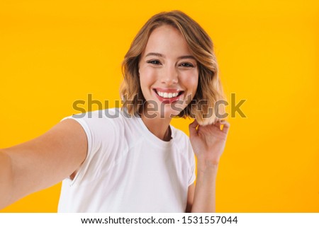 Image of alluring blond woman in basic t-shirt smiling and taking selfie photo isolated over yellow background