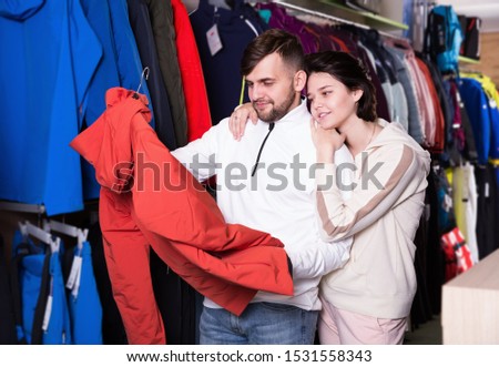 Smiling young couple choosing together modern skiwear in store