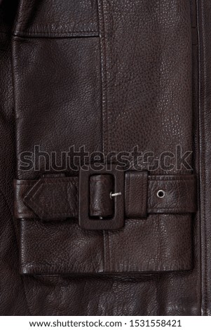 Dark brown leather sleeve with belt and clasp. Natural textured material closeup.