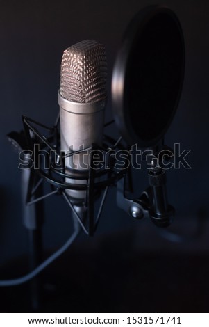 Silver studio microphone that stands out against the black background mounted with an anti-pop filter. In vertical.