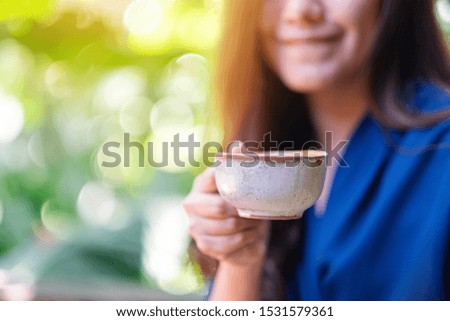Closeup image of an Asian woman holding and drinking hot coffee in the garden