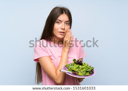 Young woman with salad over isolated blue background whispering something