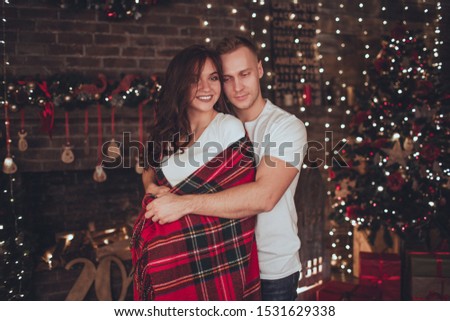 Lovely couple woman and man are covered in blanket at home near fireplace. Christmas time.