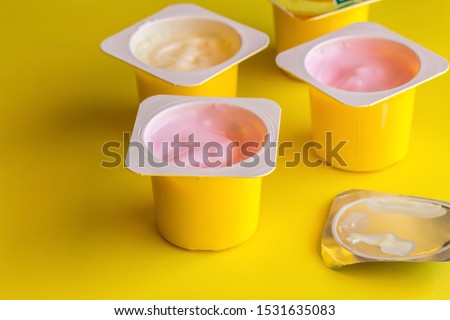 Fruit flavoured yogurt in yellow plastic cups on bright yellow background with silver foil lid - Yoghurt cup background with selective focus Royalty-Free Stock Photo #1531635083