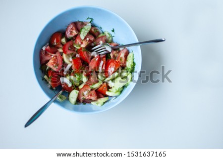 salad with tomato, cucumbers and greens in a blue bowl on a white background