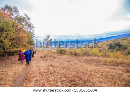 Group of active people hiking on the rainy autumn day wearing a raincoat. Real unrecognizable hikers, rearview, cloudy sky in the background.
