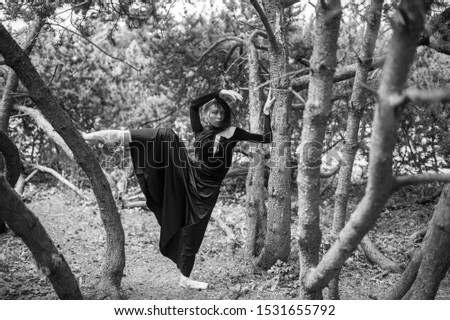 Young beautiful ballerina in black vintage dress with veil posing among trees outdoor.