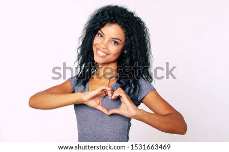 Thank you! Close-up portrait of content Afro ethnic girl with messy raven black hair standing smiling broadly, with her palms near her chest showing a hand heart.