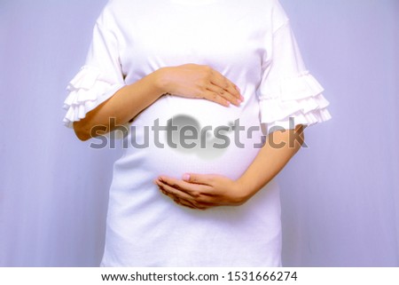 Pregnant woman in dress holds hands on belly closeup with  baby inside, conceptual motherhood image, 3D ultrasound concept