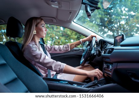 woman wheel of car changes gears on box machine. In summer autumn city. Business lady driving. Background trees. Beautiful girl everyday makeup. Business class sedan. Car sharing in city car rental