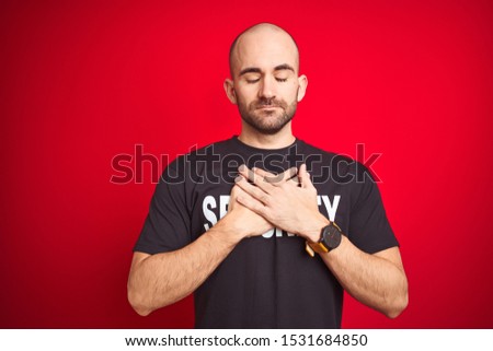 Young safeguard man wearing security uniform over red isolated background smiling with hands on chest with closed eyes and grateful gesture on face. Health concept.