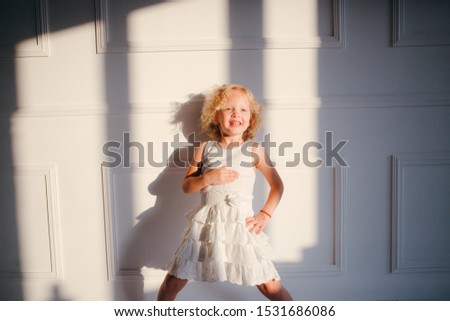 A curly blonde girl in white dress shows she is full, hand on the tummy