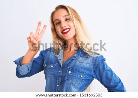 Young beautiful woman wearing casual denim shirt standing over isolated white background smiling looking to the camera showing fingers doing victory sign. Number two.