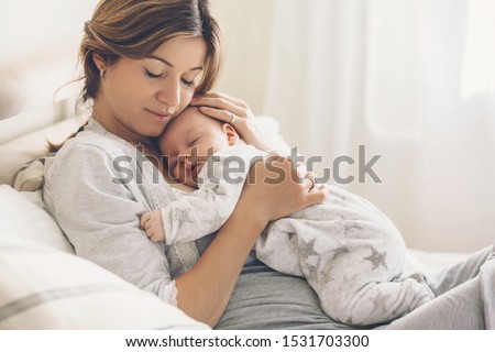 Loving mom carying of her newborn baby at home. Bright portrait of happy mum holding sleeping infant child on hands. Mother hugging her little 2 months old son. Royalty-Free Stock Photo #1531703300