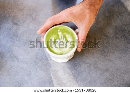 Male hand putting on table vegan matcha cappuccino with oat milk with latte art in outdoor cafe.