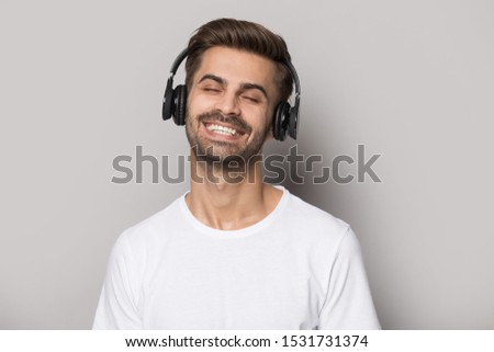 Happy caucasian man isolated on grey studio background listen to music in earphones, smiling male in white t-shirt relax enjoy quality sound in modern headphones, technology concept