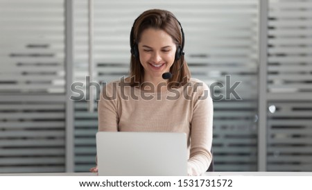 Smiling businesswoman in headset using laptop, looking at screen, call center operator agent in headphones with microphone consulting client customer, student learning online