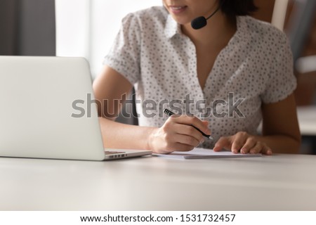 Asian woman in headset using laptop, making notes close up, employee watching webinar, student in headphones with microphone learning language online, listening translating lecture course