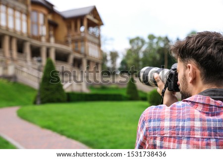 Photographer taking photo of beautiful house with professional camera outdoors