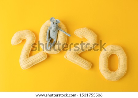 Happy New Year 2020. Number 2020 knitted from yarn and gray toy mouse symbol of year on bright yellow background, cheese color. Flat lay, top view, copy space