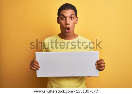 Young handsome arab man holding banner standing over isolated yellow background scared in shock with a surprise face, afraid and excited with fear expression