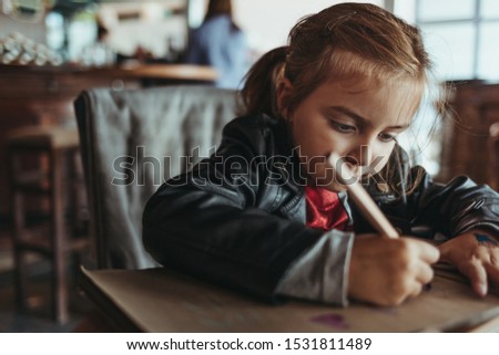 Adorable preschool girl drawing with wooden pencils in a cozy cafe. Cute daughter smiling and drawing colorful shapes for kindergarten homework