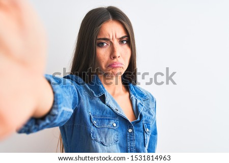 Beautiful woman wearing denim shirt make selfie by camera over isolated white background depressed and worry for distress, crying angry and afraid. Sad expression.