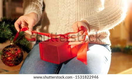 Closeup image of young mother packing Christmas gifts for her children. Woman tying ribbon box on present box.