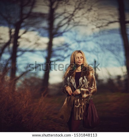 Outdoor fashion art photo of young beautiful blonde woman surrounded autumn leaves outdoor in park. Autumn season fashion concept