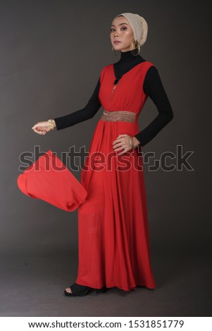 Beautiful female model wearing black inner and red dress with hijab, a modern lifestyle outfit  for Muslim woman isolated over grey background. Stylish hijab fashion lifestyle portraiture concept.