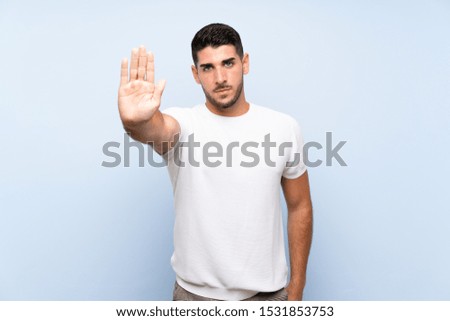 Caucasian handsome man over isolated blue background making stop gesture
