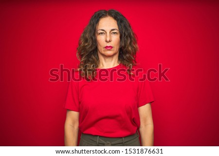 Middle age senior woman with curly hair over red isolated background with serious expression on face. Simple and natural looking at the camera.