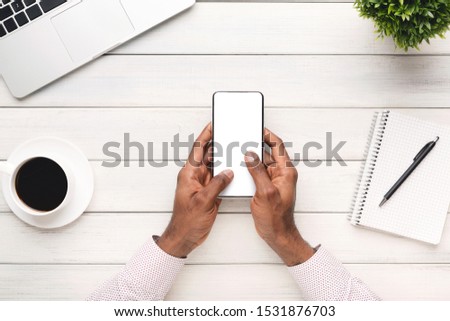 African american man using modern smartphone with empty white screen at workplace, copy space