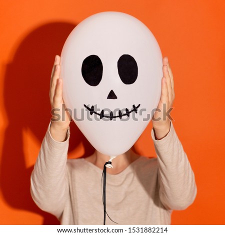 Halloween costume party. Close up of ghost balloon hiding woman face on orange background