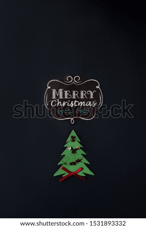 Black background with chalk message Merry Christmas, Christmas tree cut out, golden and red ornaments, red ribbon.