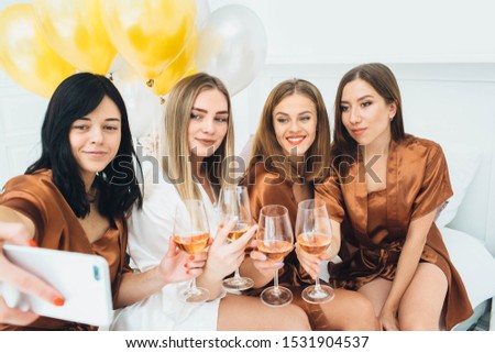 girlfriends wearing satin robes celebrating hen party . Women drinking alcohol and making selfie together
