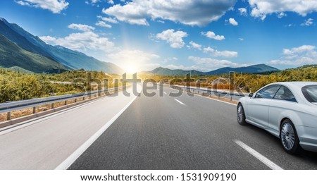 White car moves on the road among the mountains and forests.