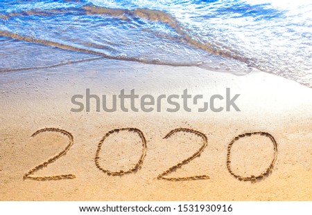Happy New Year 2020! Text, lettering on sand on beach with blue wave, sea shore, clear ocean. Numbers written on golden sunny sand. Handwritten inscription. Vacation at new year concept. Summer, sunny