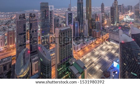 Skyline of the buildings near Sheikh Zayed Road and DIFC aerial night to day transition timelapse in Dubai, UAE. Modern towers and illuminated skyscrapers in financial center and downtown before