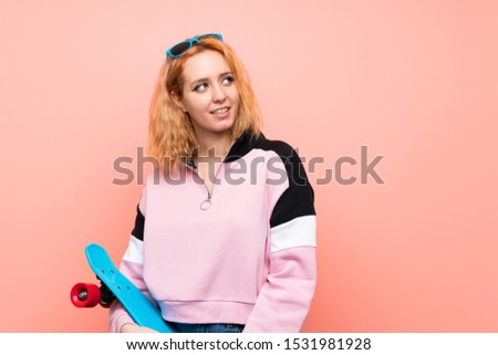 Young skater woman over isolated pink background laughing and looking up