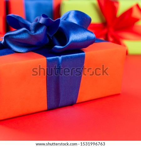 Red gift box with a blue ribbon on a red background. Lots of Christmas gift boxes.