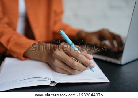 Closeup shot of university student hand using pen and writing in notebook, exam preparation, presentation, working project at workplace. Education concept. Woman taking notes, typing on keyboard  Royalty-Free Stock Photo #1532044976