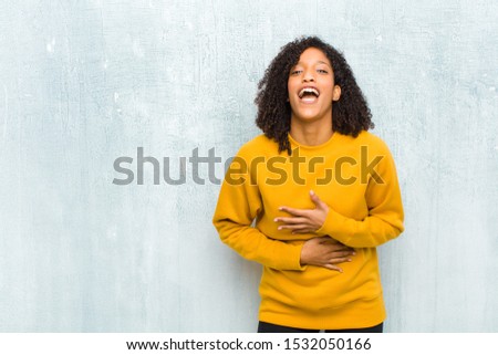 young pretty black woman laughing out loud at some hilarious joke, feeling happy and cheerful, having fun