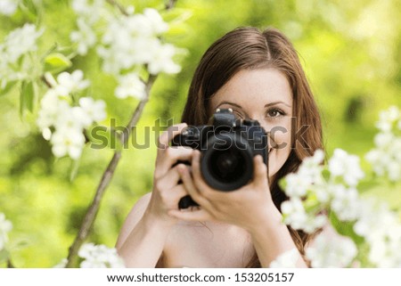 Portrait of beautiful brunette girl making photos at summer green park.